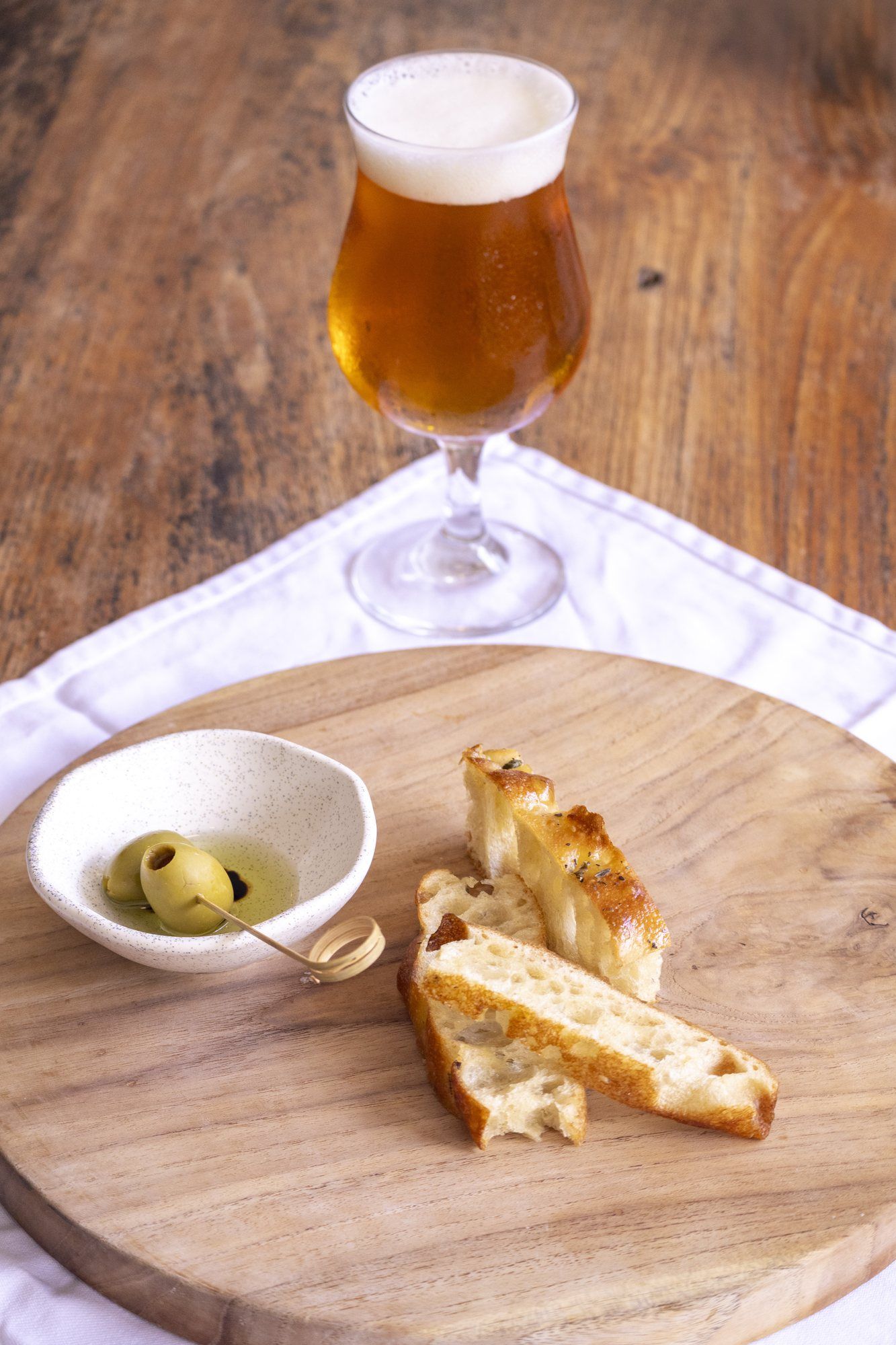 A glass of beer next to olives and focaccia on a wooden board