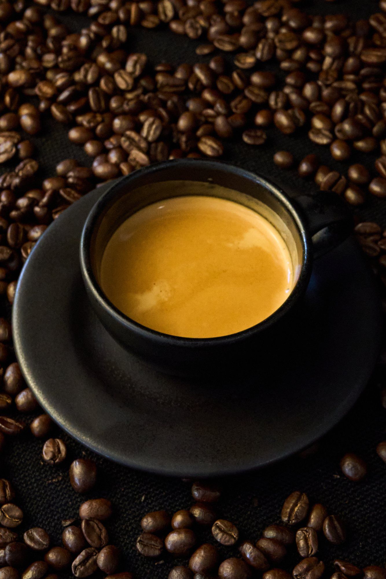 Espresso in a black cup, surrounded by coffee beans