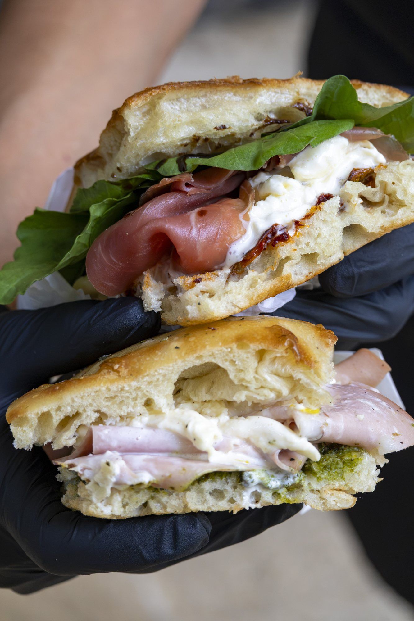 Two focaccia sandwiches held in gloved hands