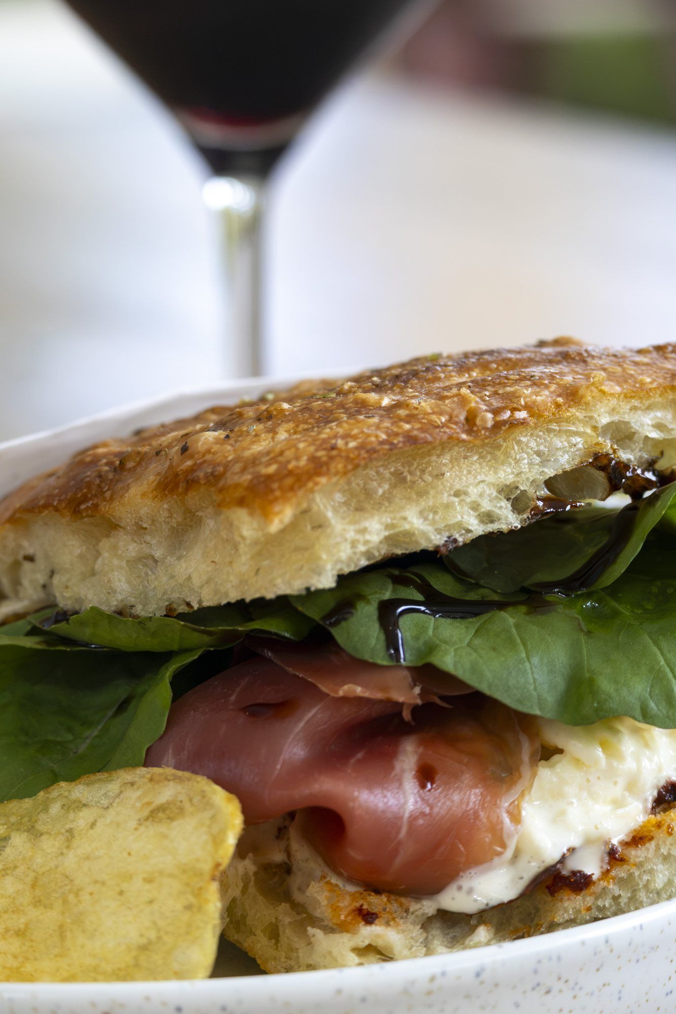 Focaccia sandwich with prosciutto and greens, wine behind